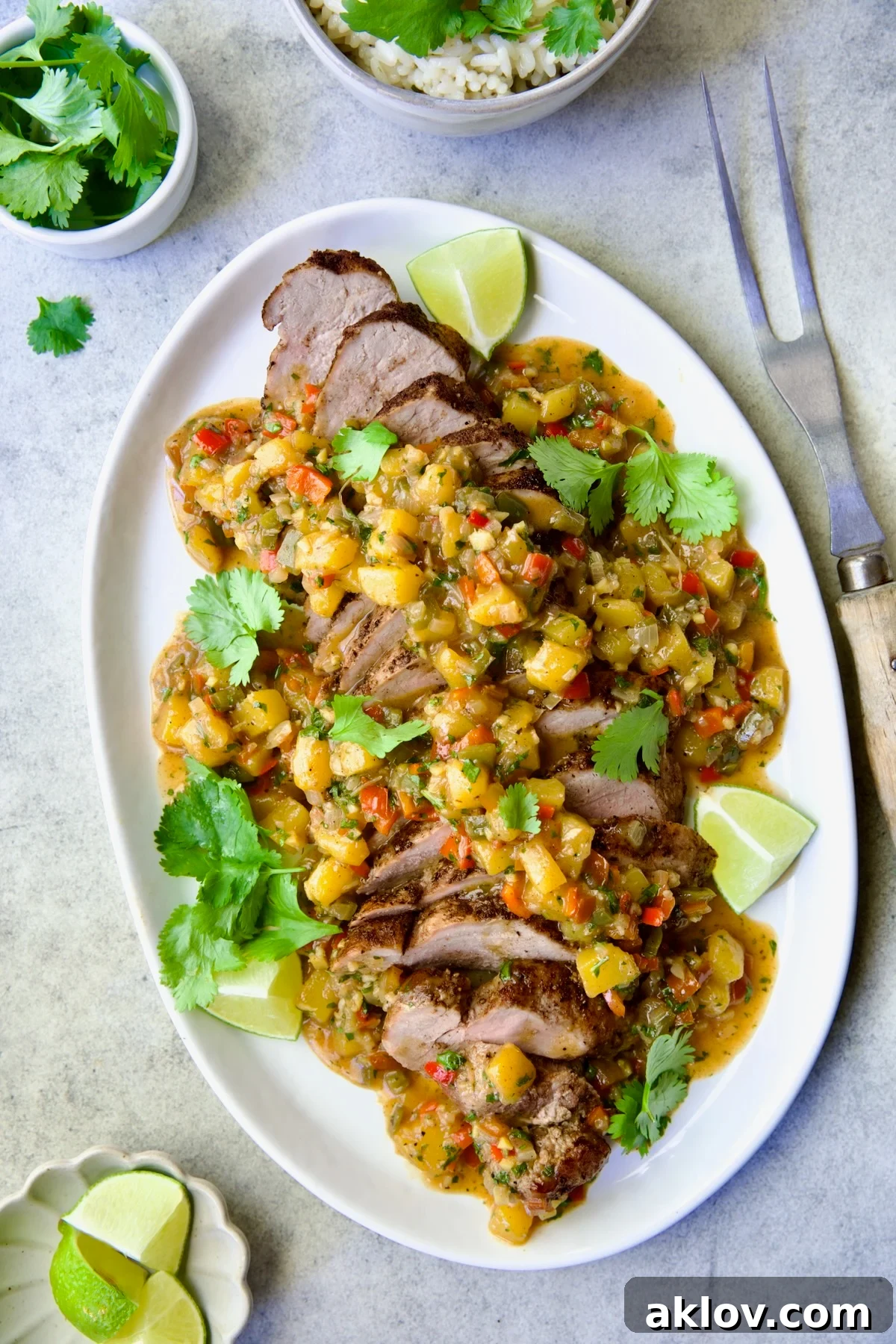 Sliced and sauced Caribbean Pork Tenderloin on white oval platter garnished with cilantro and lime wedges.