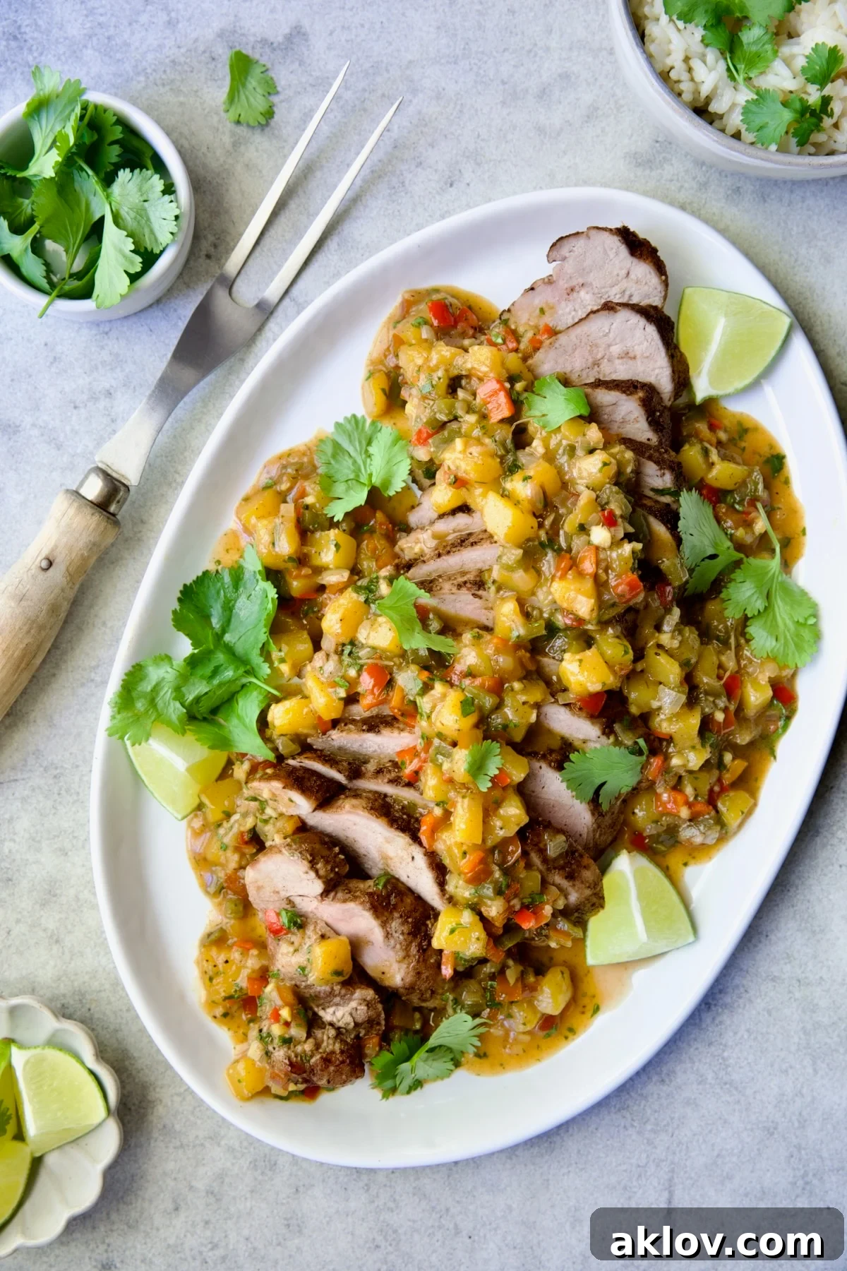 Sliced and sauced Caribbean Pork Tenderloin on white oval platter garnished with cilantro and lime wedges.
