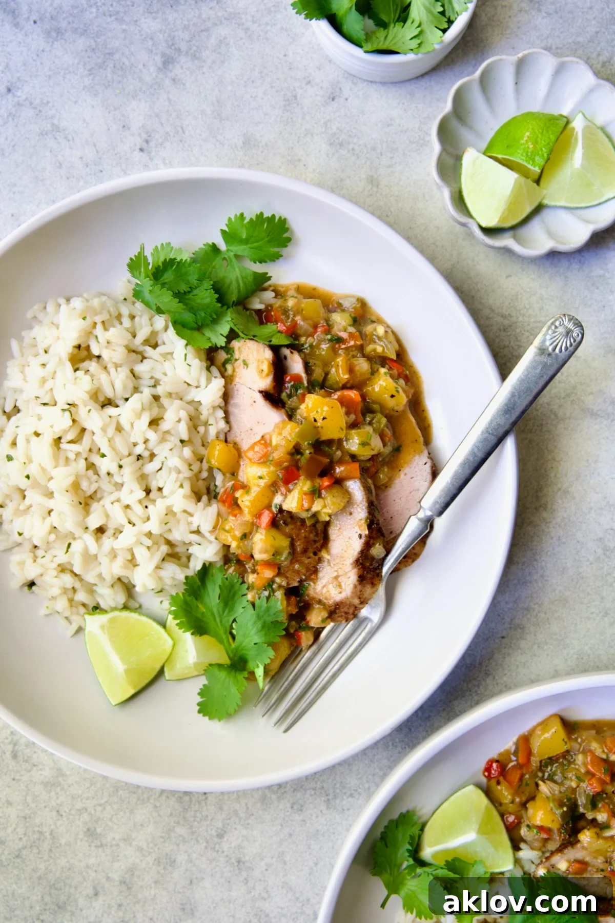 One serving of sliced and sauced Caribbean Pork Tenderloin in white dinner bowl garnished with cilantro and lime wedges.