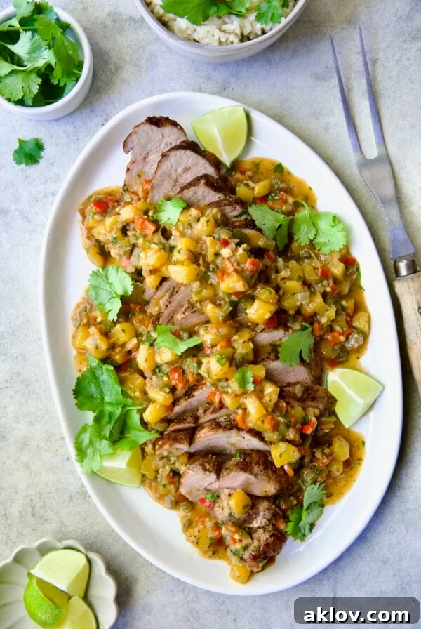 Sliced and sauced Caribbean Pork Tenderloin on white oval platter garnished with cilantro and lime wedges.