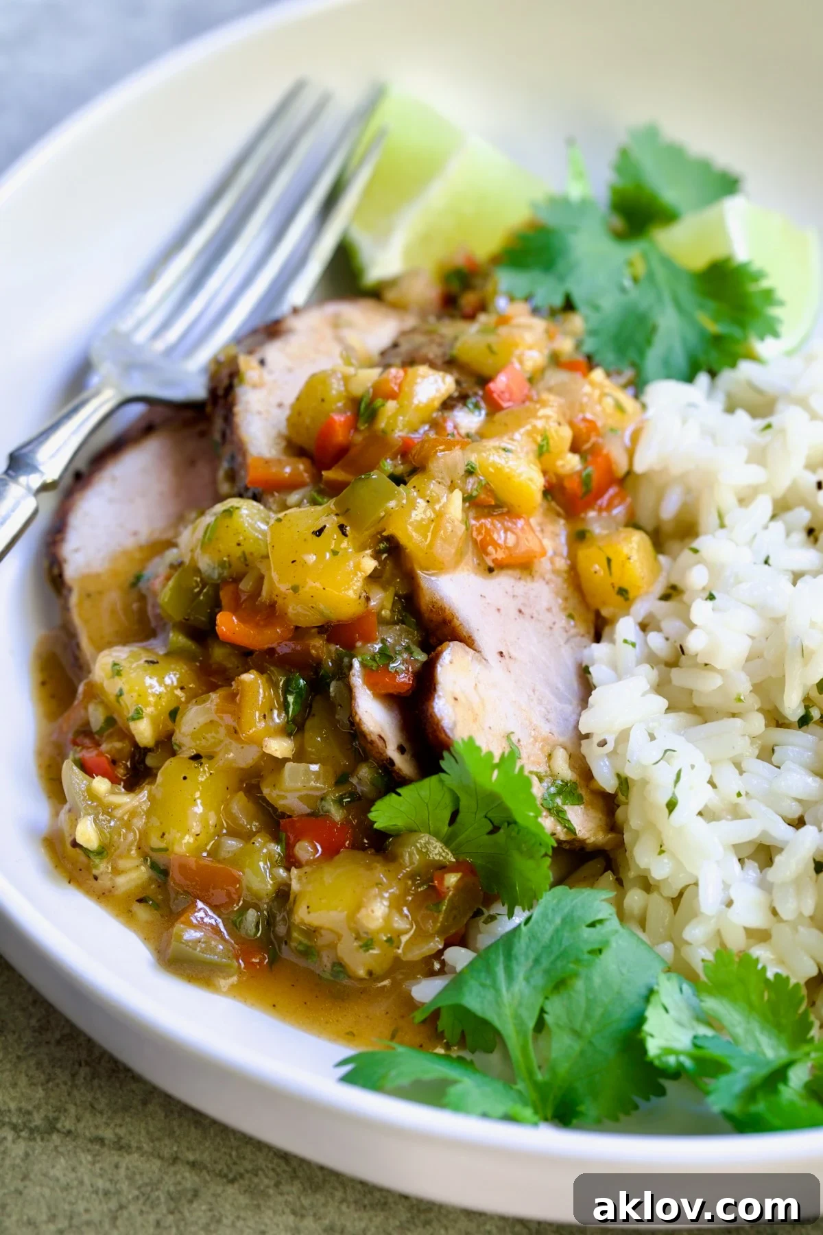 One serving of sliced and sauced Caribbean Pork Tenderloin in white dinner bowl garnished with cilantro and lime wedges.