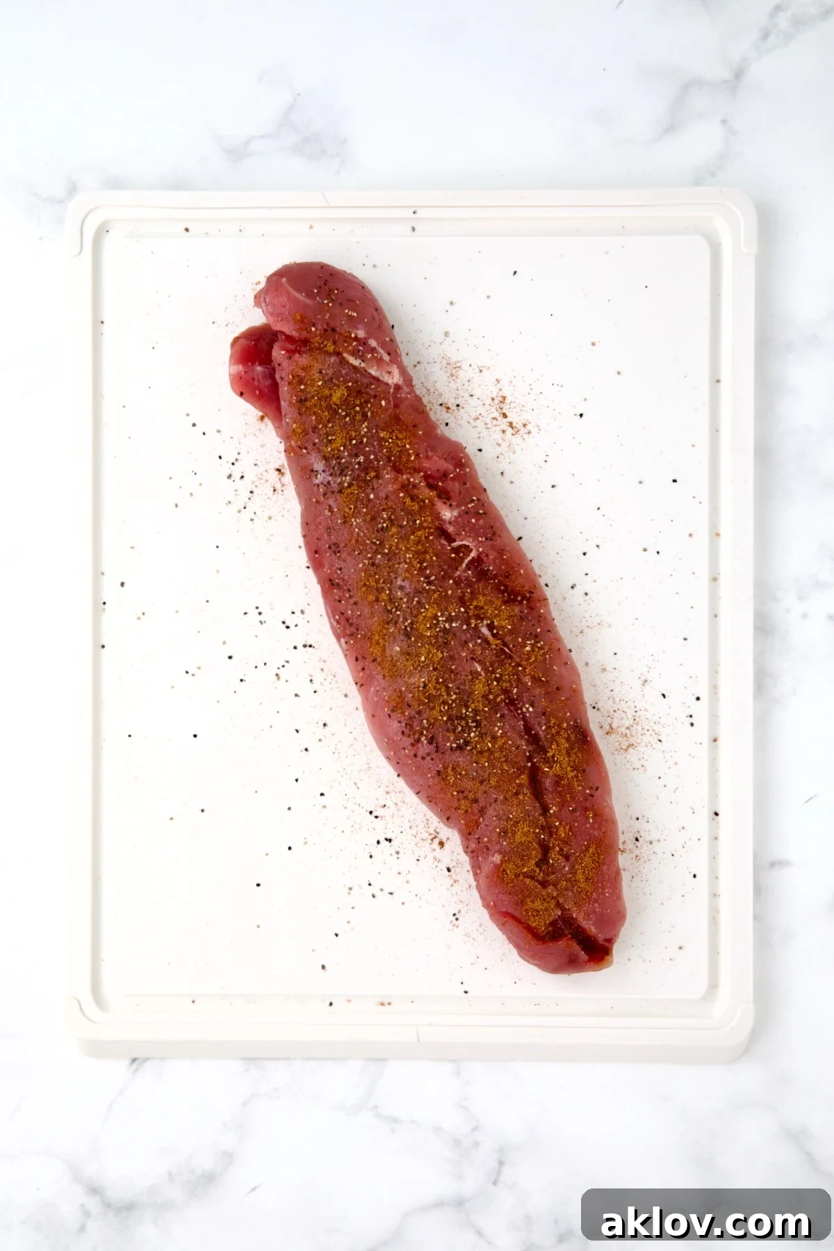 Seasoned pork tenderloin on white plastic cutting board.