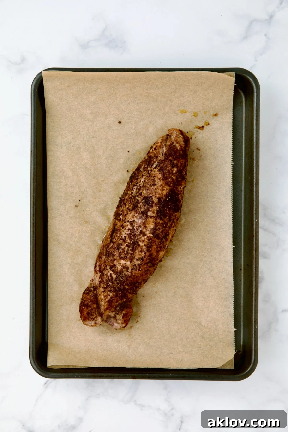 Baked pork tenderloin on brown parchment paper on rimmed baking sheet.