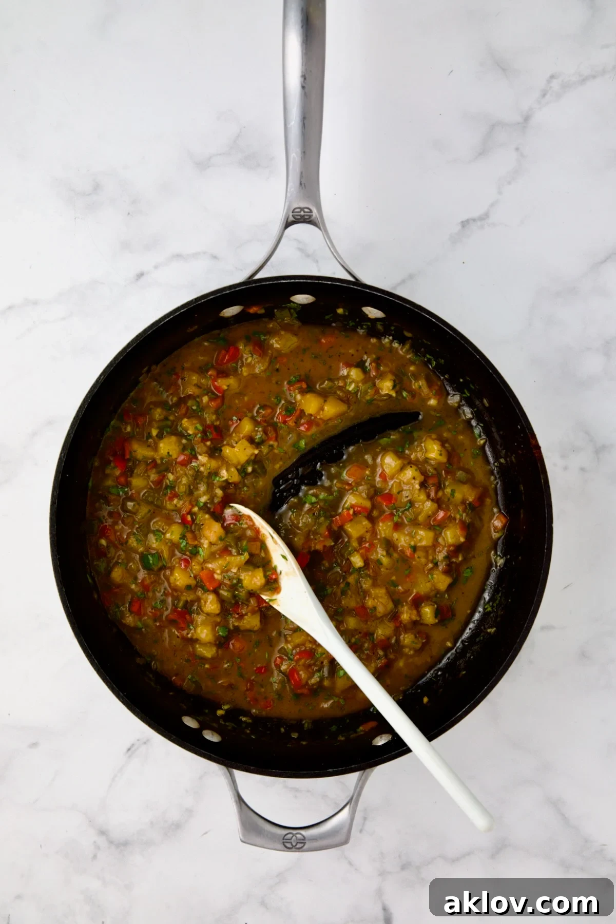 Finished mango sauce in nonstick skillet being stirred with white mixing spoon.