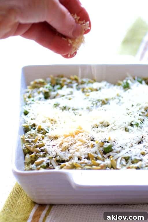 Vibrant Pesto Orzo Bake with Garden Peas 4 Photo of cheese being sprinkled over Baked Orzo with Pesto Peas Prosciutto and Mascarpone before being baked.