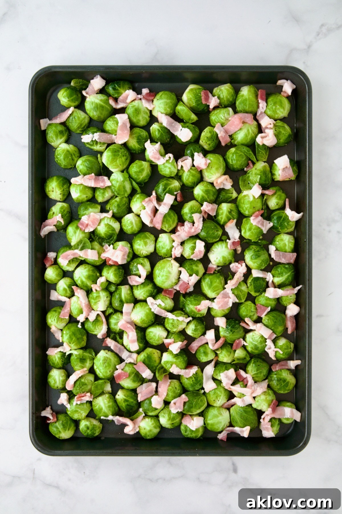 Halved Brussels sprouts on rimmed sheet pan with diced bacon.