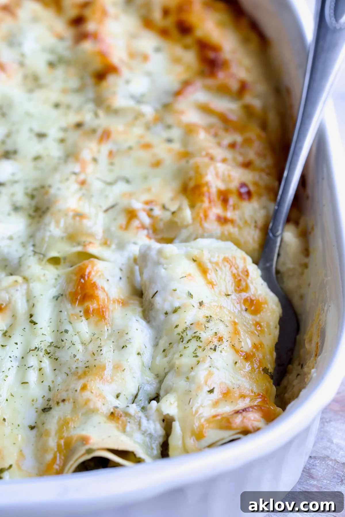 Serving fork picking up a Cannelloni with Chicken, Spinach and Artichokes from white baking dish.