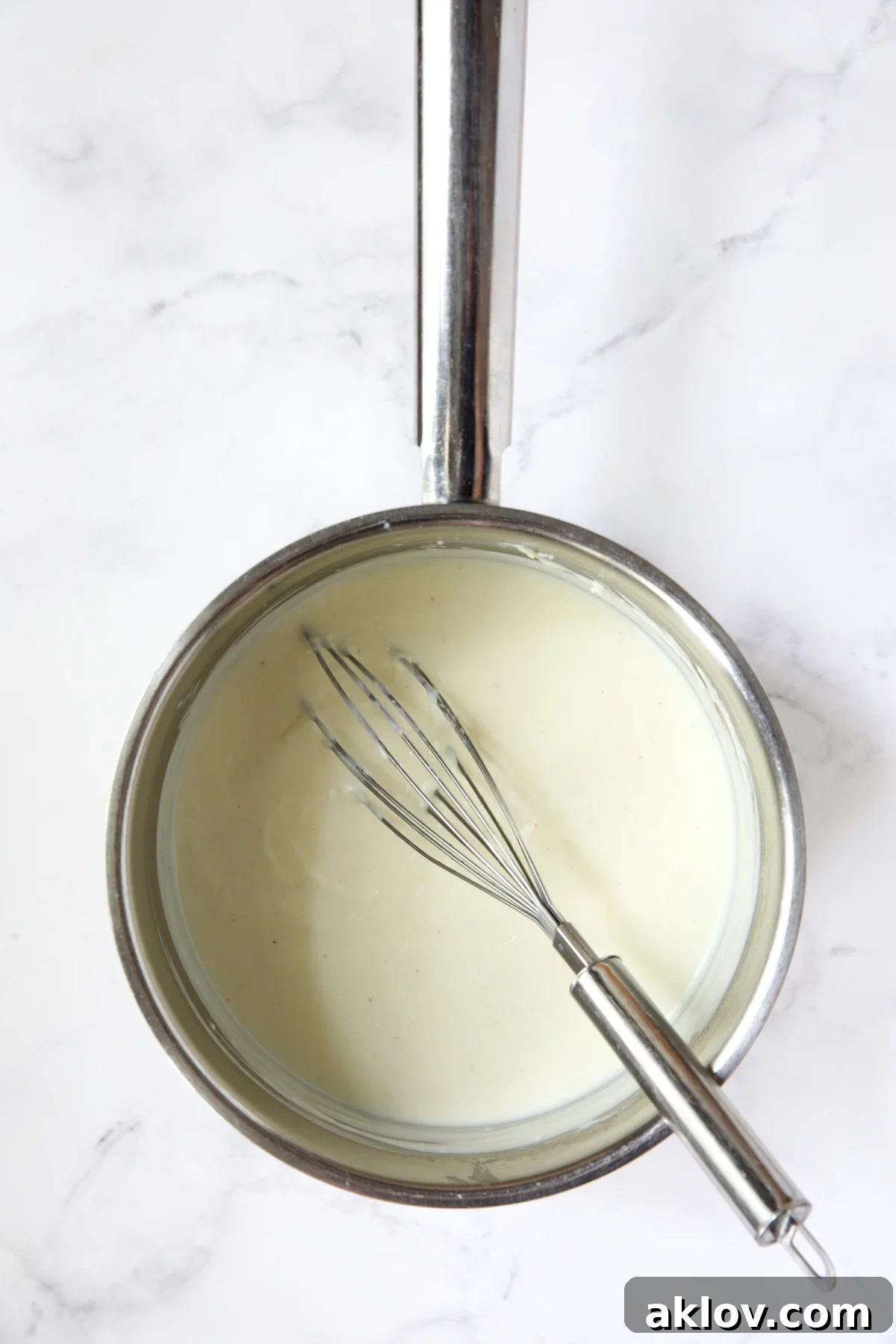 Bechamel sauce in stainless steel saucepan with wire whisk.