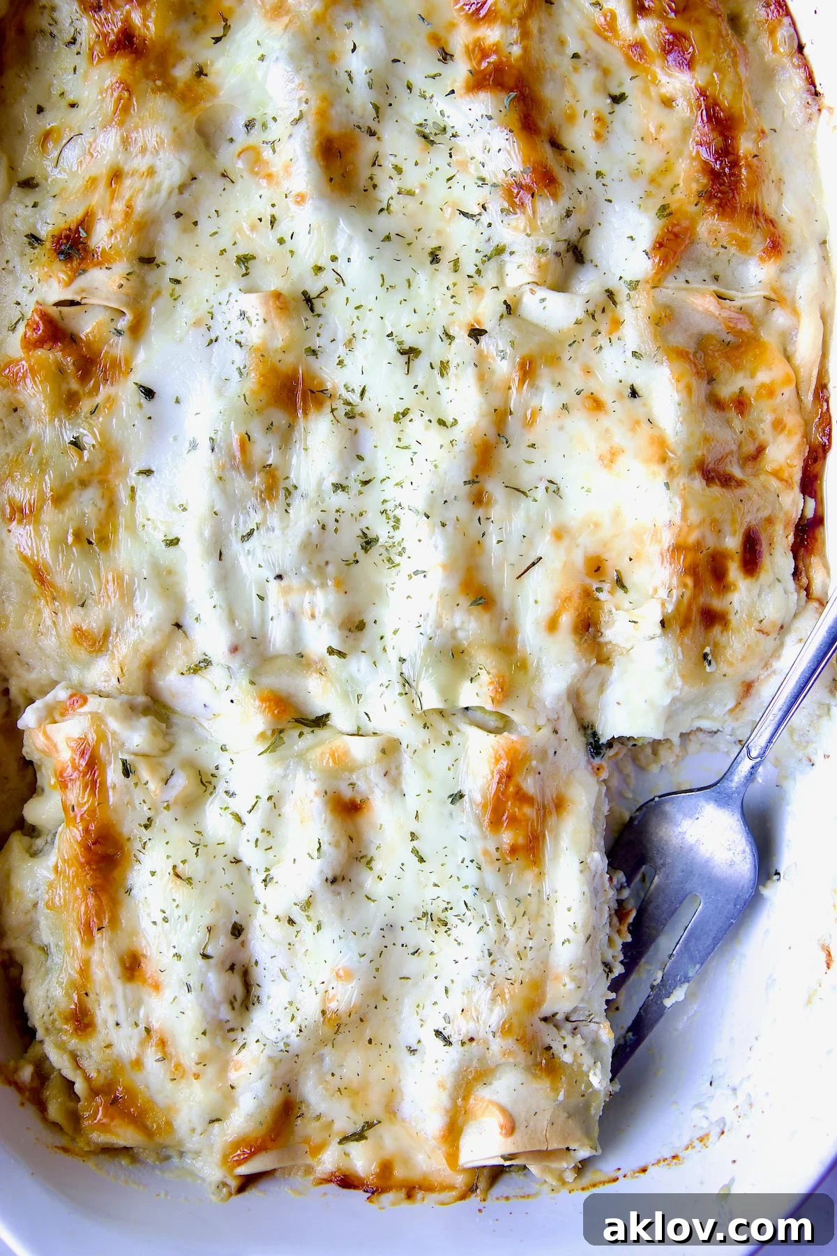 Cannelloni with Chicken, Spinach and Artichokes in white baking dish with one piece missing and serving fork in its place.