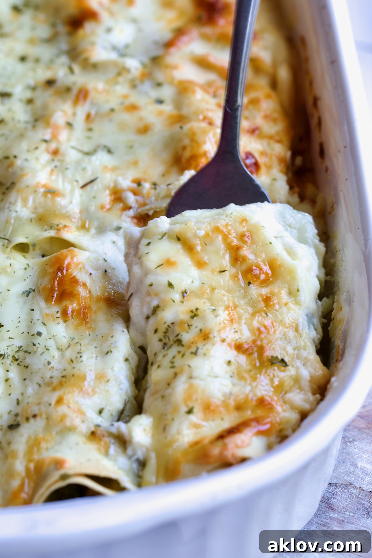 Serving fork picking up a Cannelloni with Chicken, Spinach and Artichokes from white baking dish.