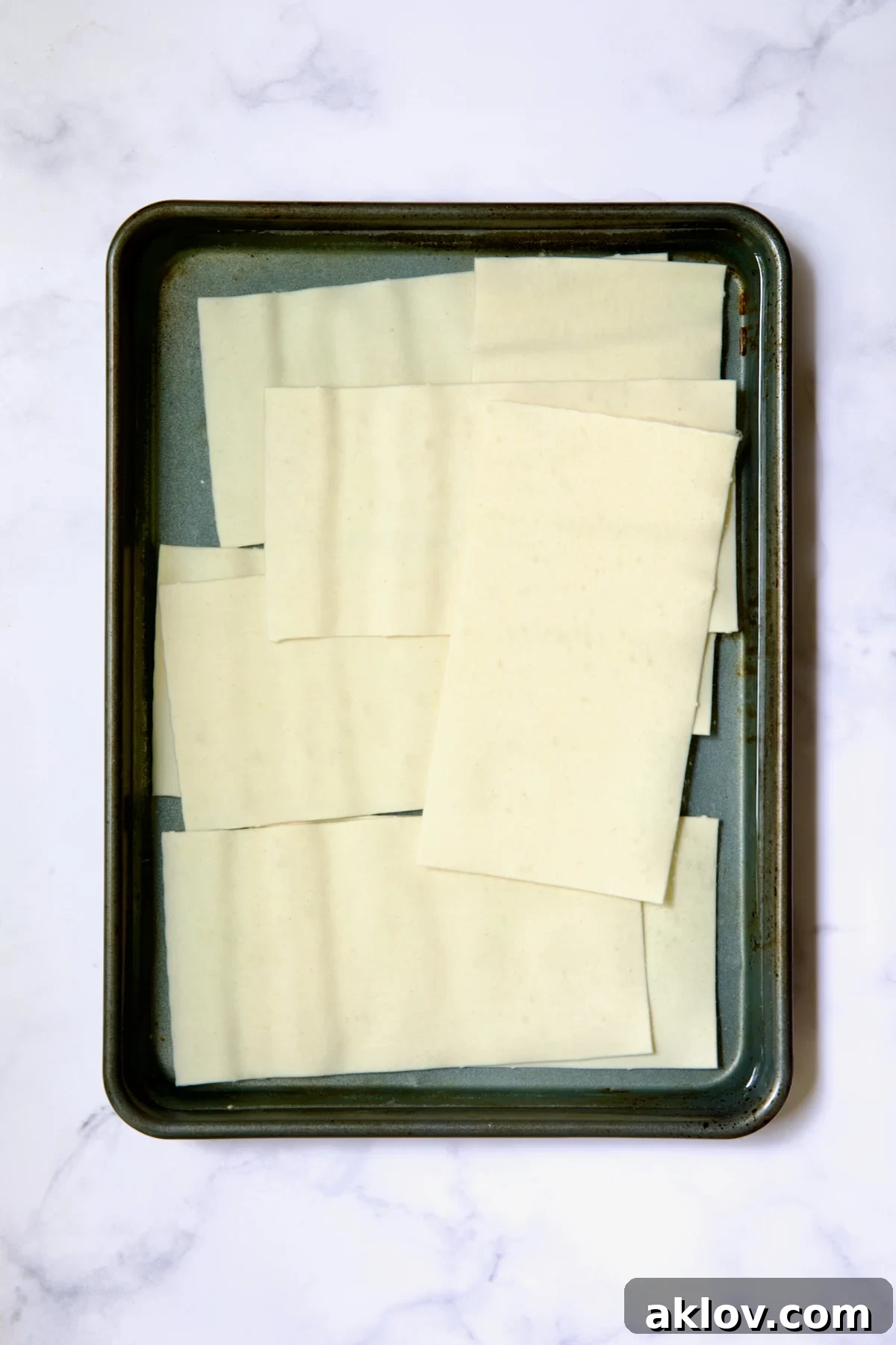 12 flat lasagna sheets in water in rimmed sheet pan.