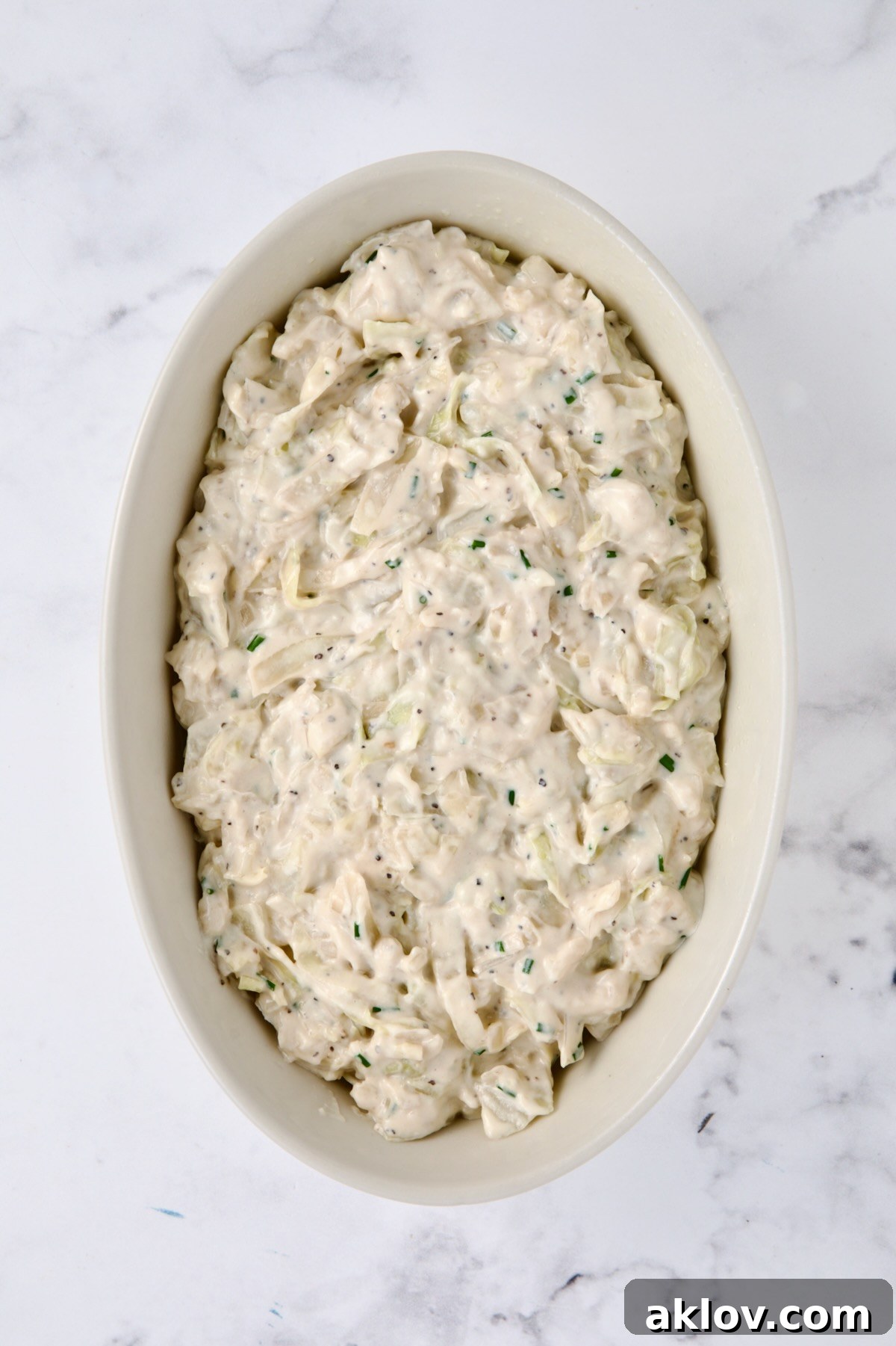 The creamy cabbage mixture carefully transferred and spread into a white oval baking dish, ready for its topping and baking.