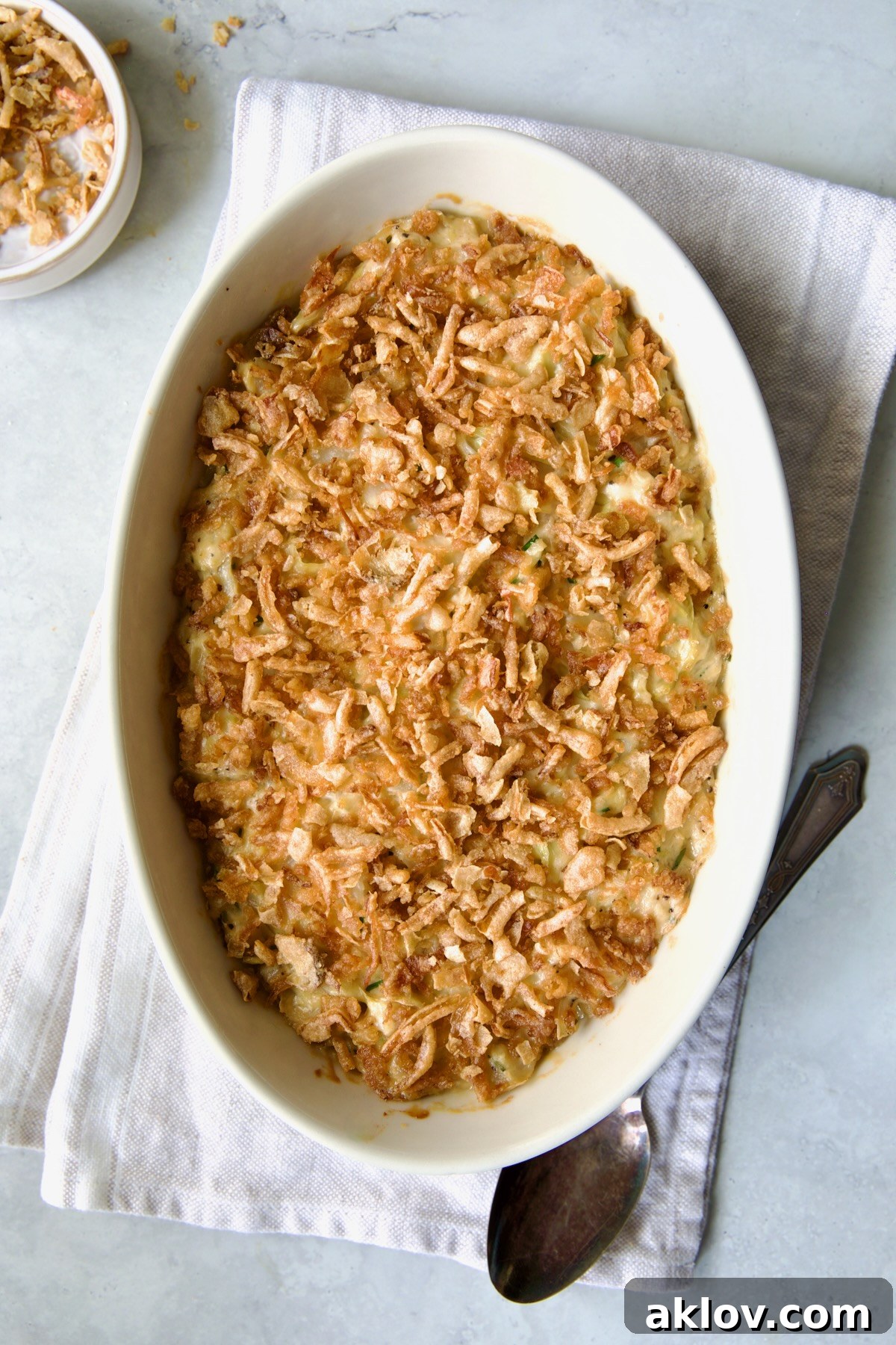 The finished Creamed Cabbage Casserole, baked to perfection with a golden-brown crispy topping, presented in a white oval baking dish with an ornate serving spoon.