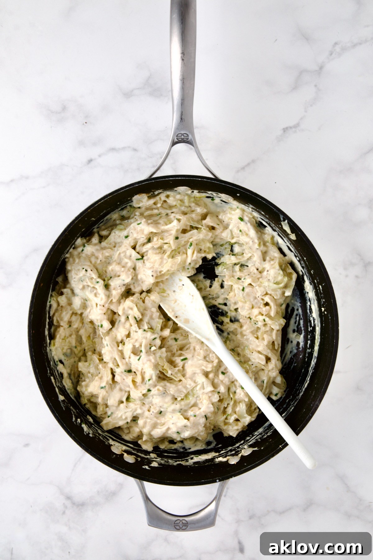 Creamed cabbage being stirred vigorously in a nonstick skillet with a white spoon, ensuring every piece is coated in the rich, savory sauce.