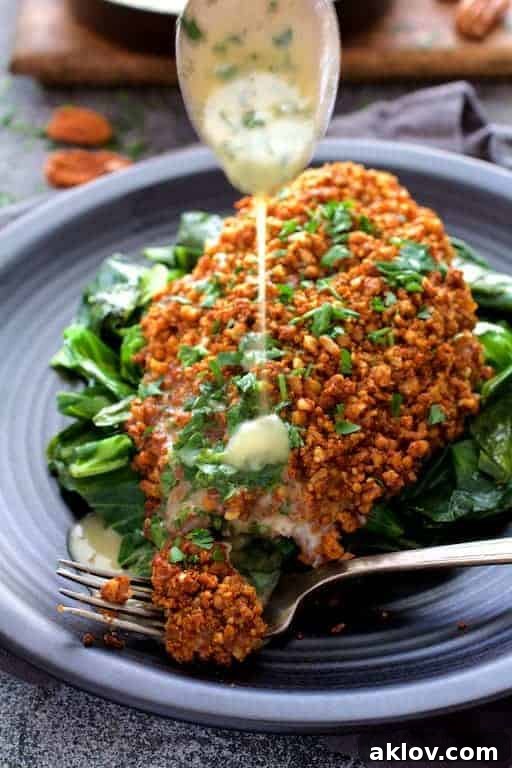 Photo of Baked Catfish Pecan Meuniere with Spicy Sauteed Greens on black plate being drizzled with lemon butter.