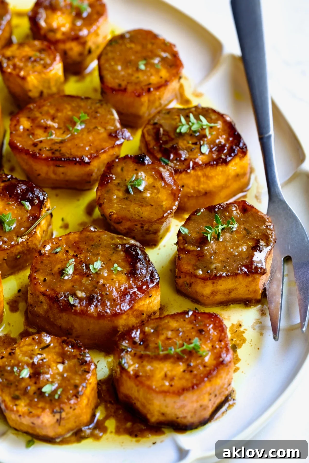 Fondant Sweet Potatoes garnished with fresh thyme on white oval platter.