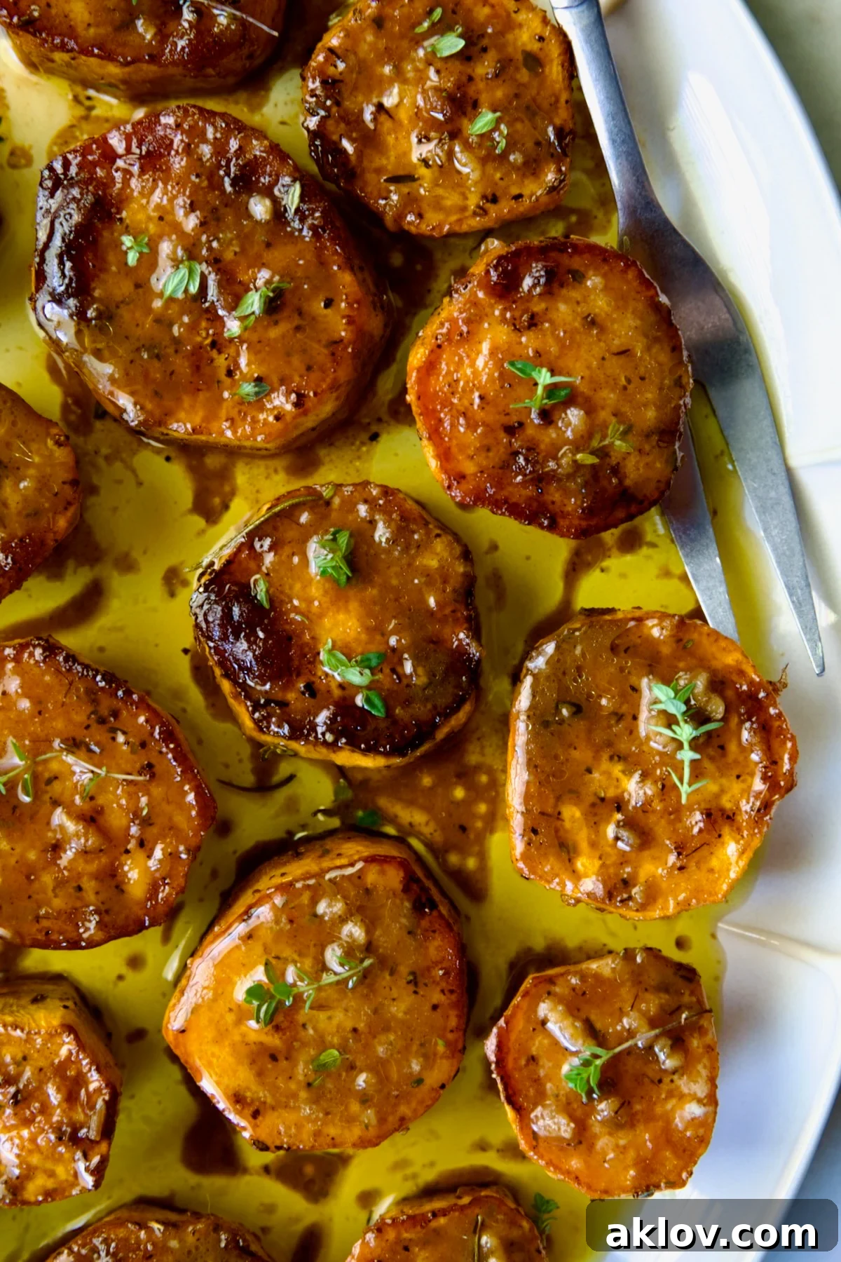 Fondant Sweet Potatoes garnished with fresh thyme on white oval platter.
