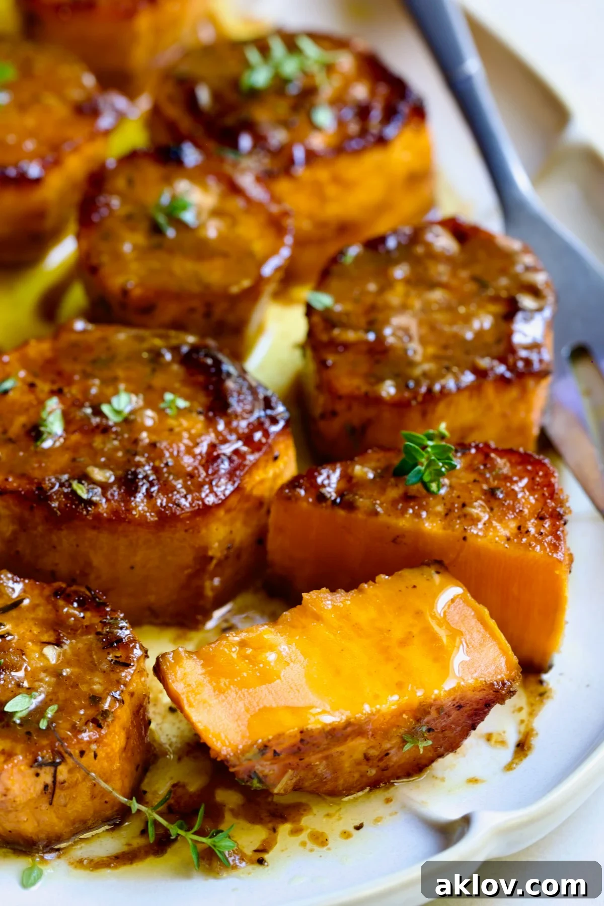 Fondant Sweet Potatoes garnished with fresh thyme on white oval platter with one cut in half.