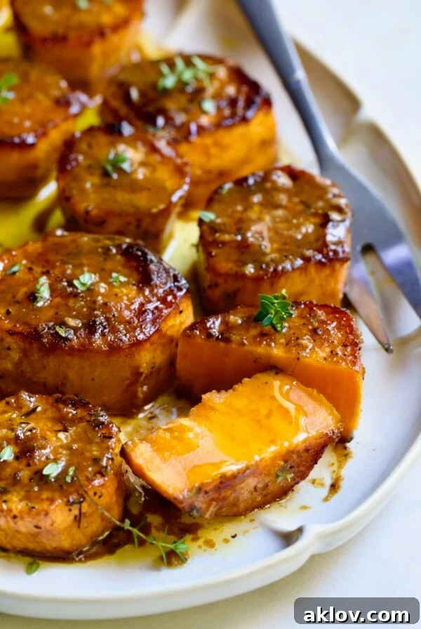 Fondant Sweet Potatoes garnished with fresh thyme on white oval platter with one cut in half.