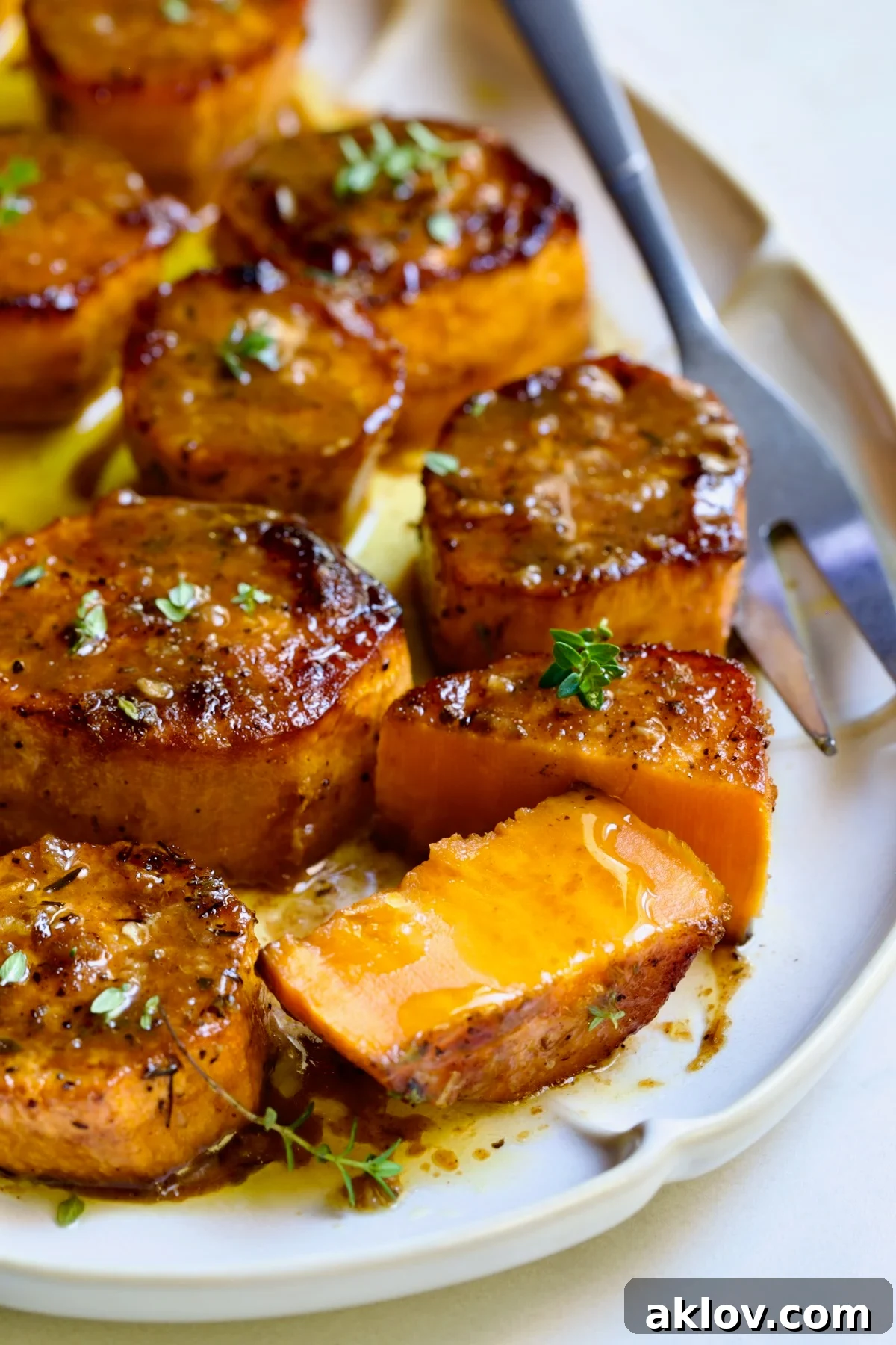 Fondant Sweet Potatoes garnished with fresh thyme on white oval platter with one cut in half.