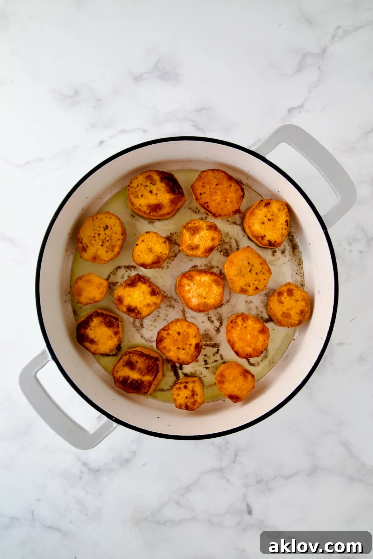 Rounds of sweet potatoes in white enamel cast iron skillet after being browned.