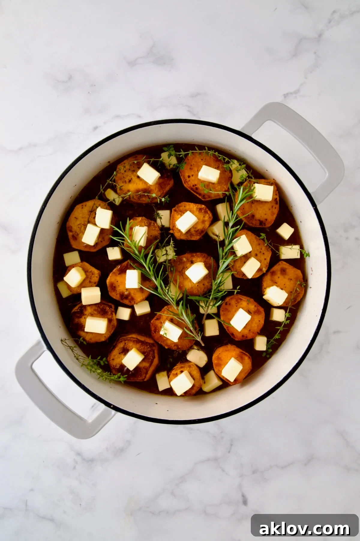 Butter and herbs added to browned sweet potato rounds in white enamel cast iron skillet.
