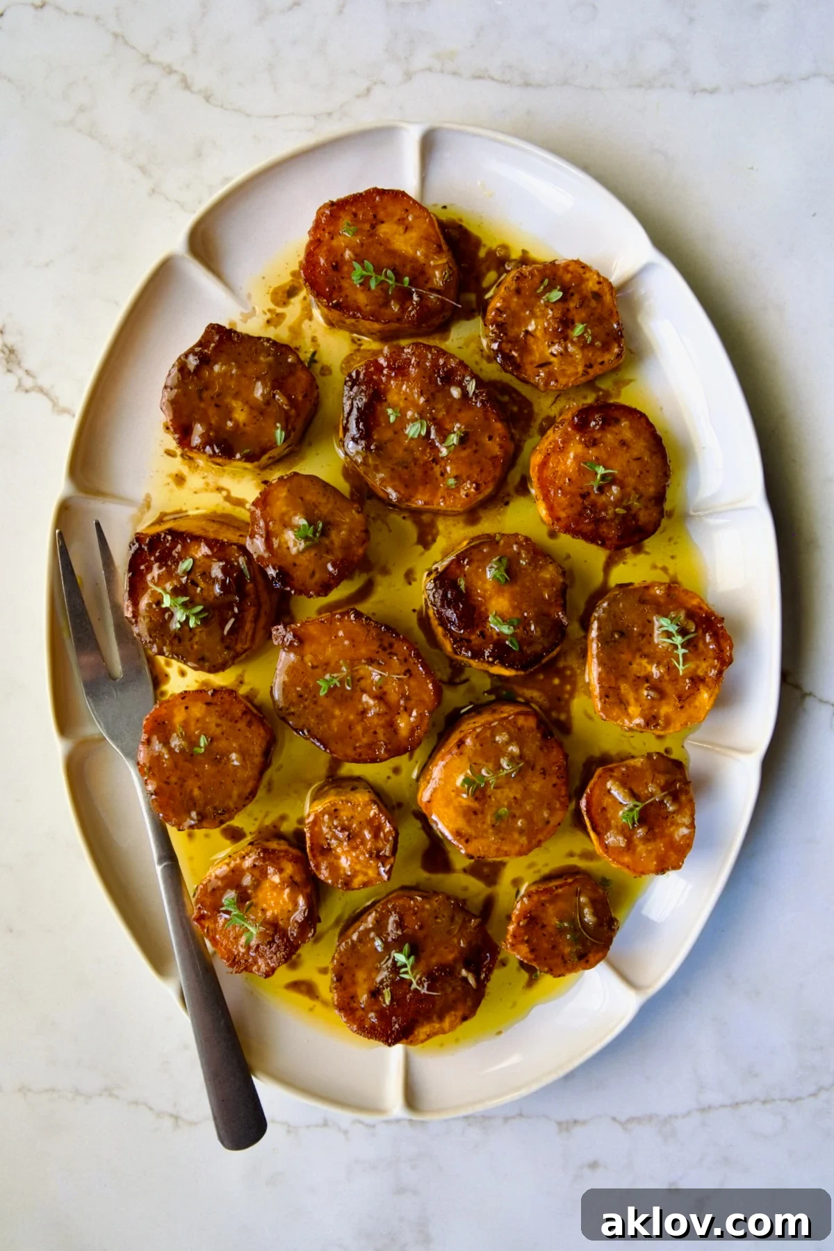 Fondant Sweet Potatoes garnished with fresh thyme on white oval platter.