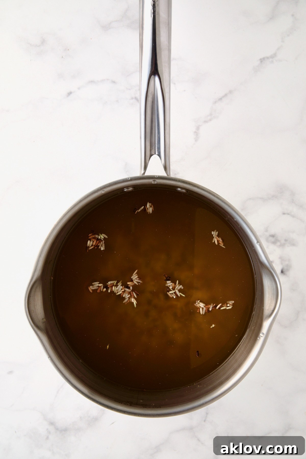 Wild rice blend simmering gently in chicken stock within a gleaming stainless steel saucepan.