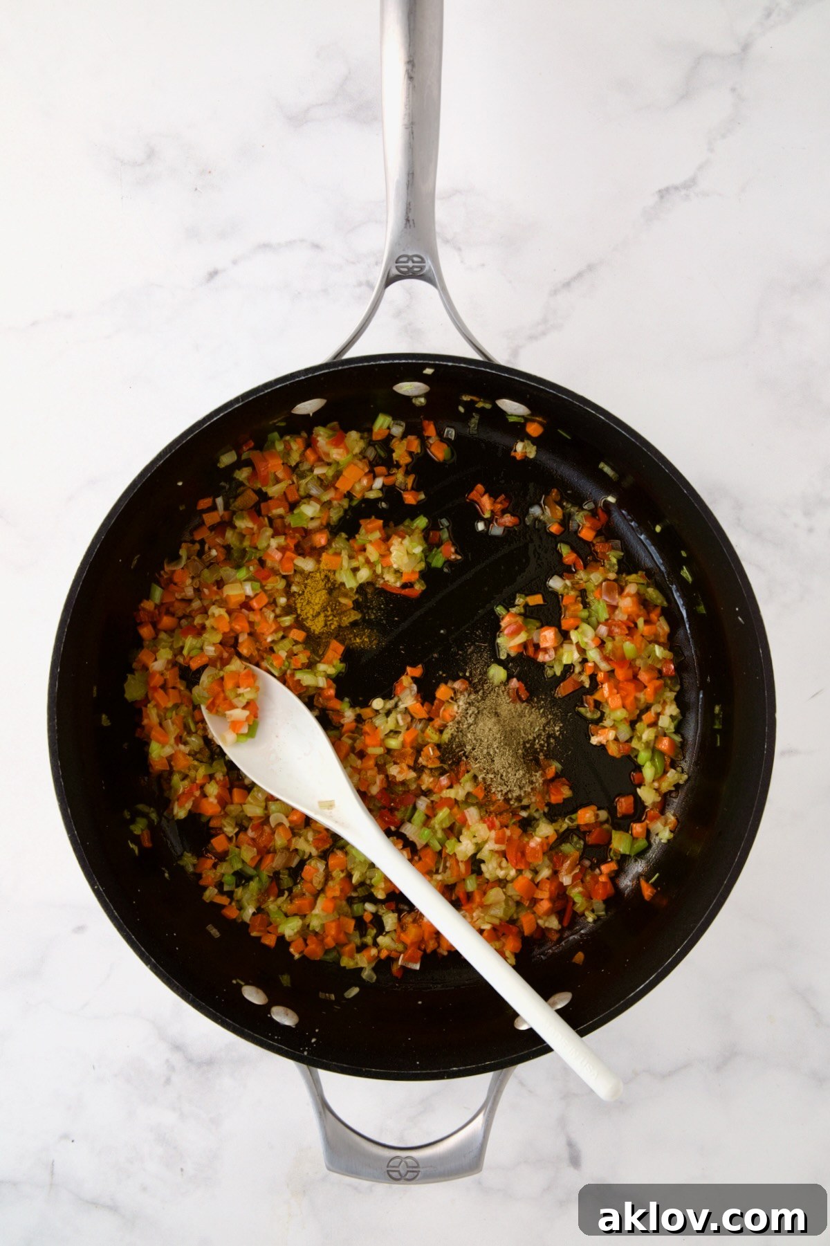 Close-up of cooked vegetables in a nonstick skillet, with poultry seasoning and curry powder freshly added and stirred in.