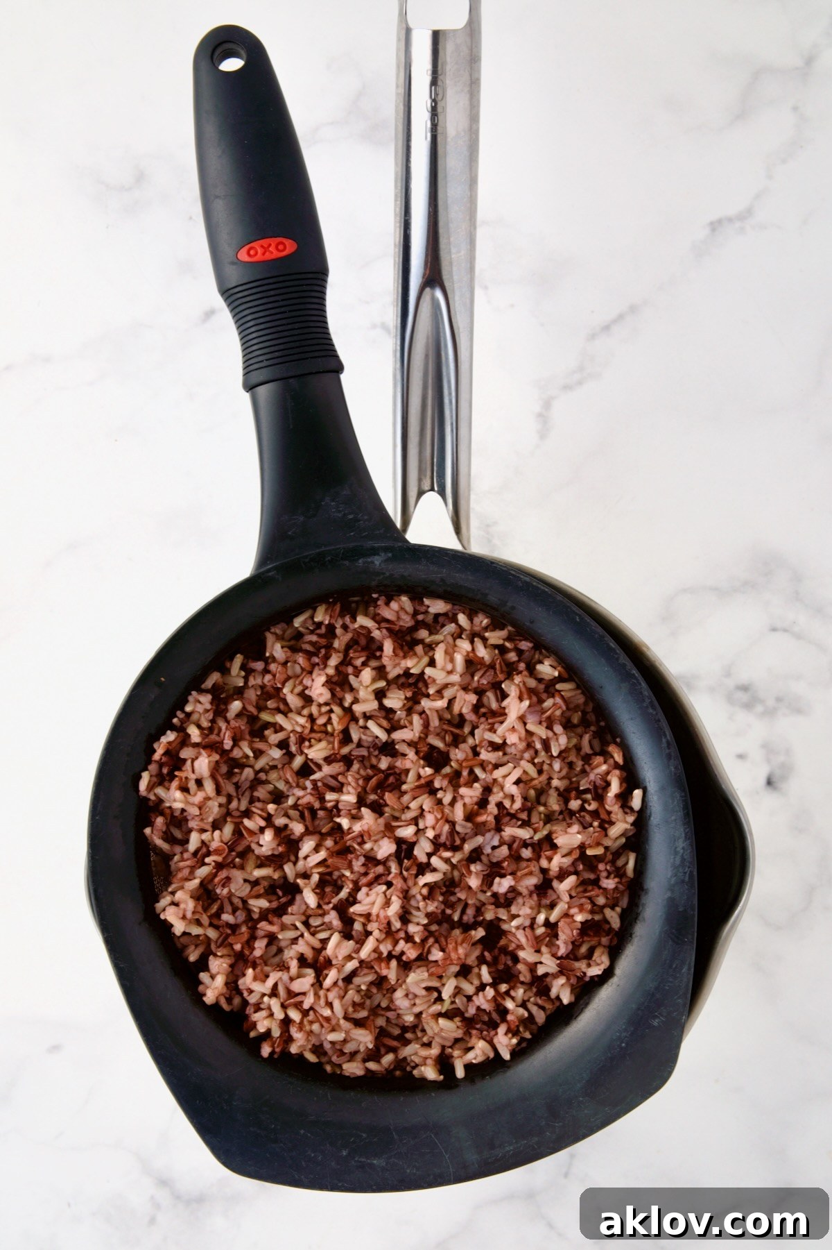 Wild rice blend being meticulously drained in a black plastic colander over a stainless steel saucepan, ensuring no excess moisture.