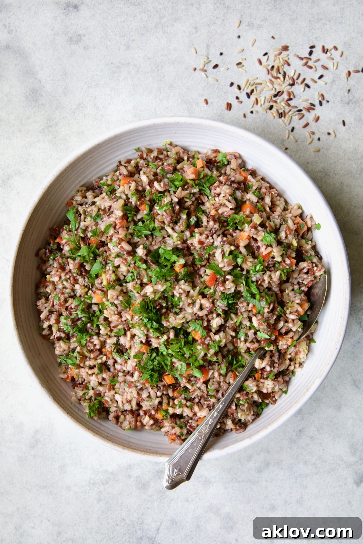 A stunning presentation of Wild Rice Pilaf in a white serving bowl, garnished with fresh parsley, with a serving spoon tucked beside it.