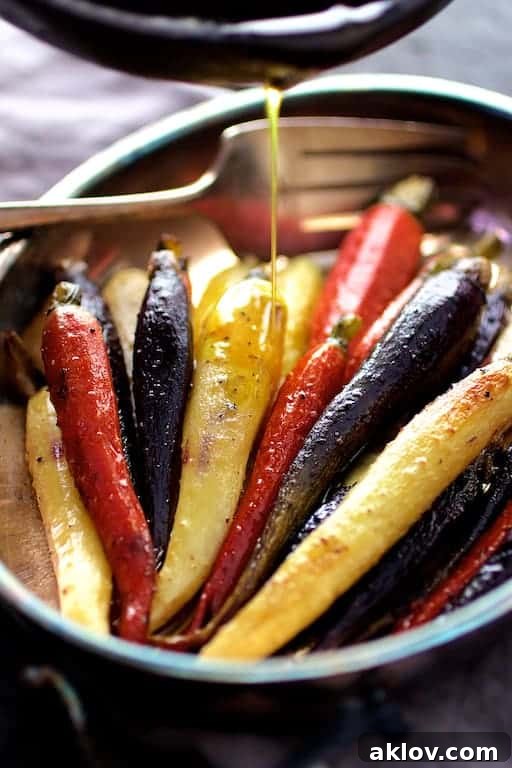 Roasted Carrots with Honey Browned Butter in an oval stainless steel baking dish, showing butter being drizzled over the vibrant carrots.