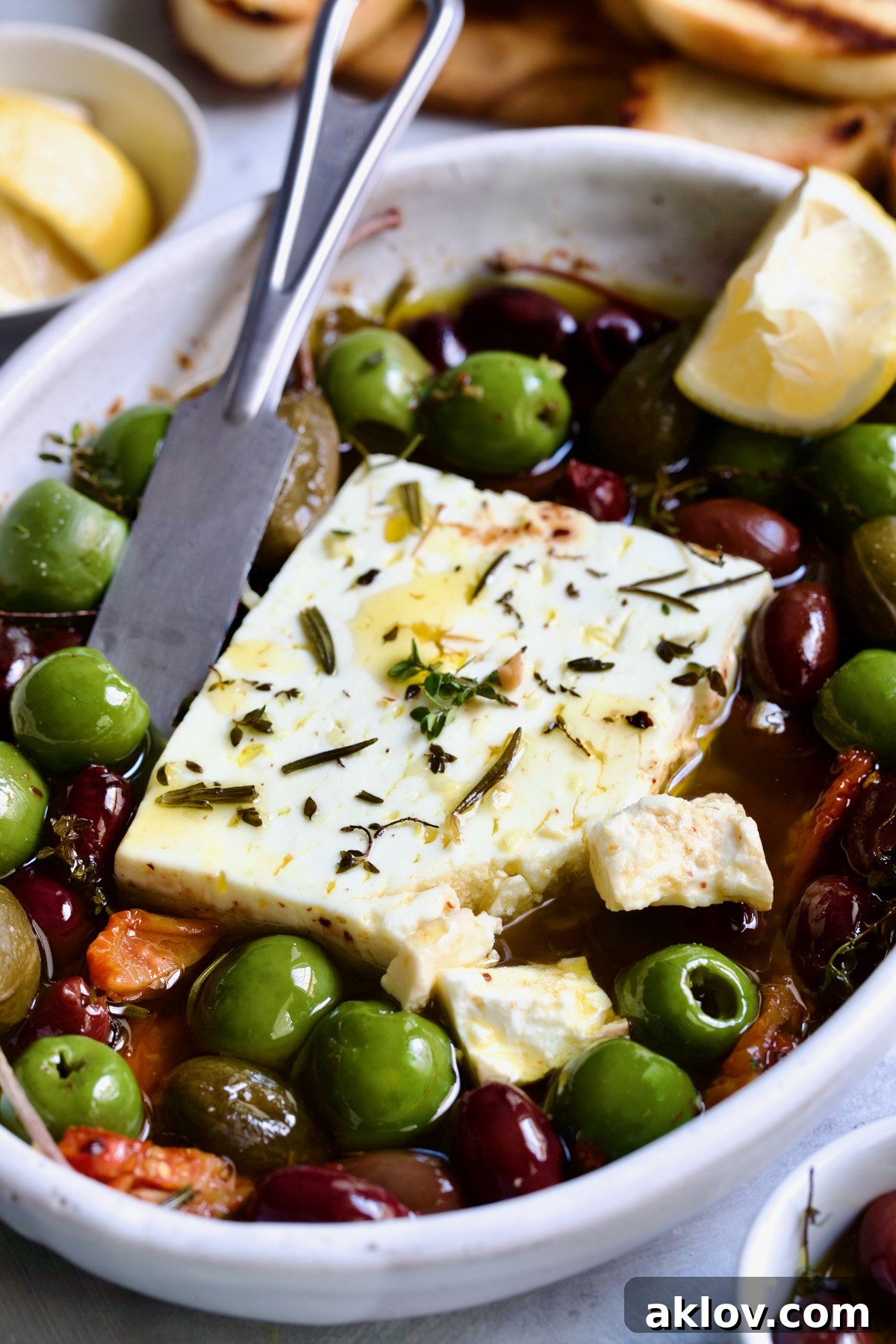 Baked Feta Cheese and Olives in white oval baking dish with serving knife.