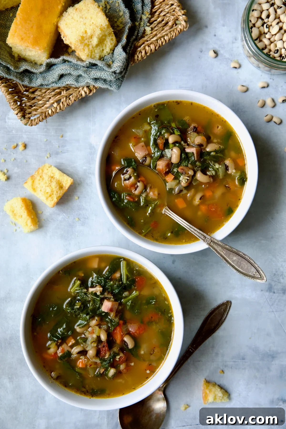 Two servings of Black-Eyed Pea Soup in white bowls with cornbread in a basket.