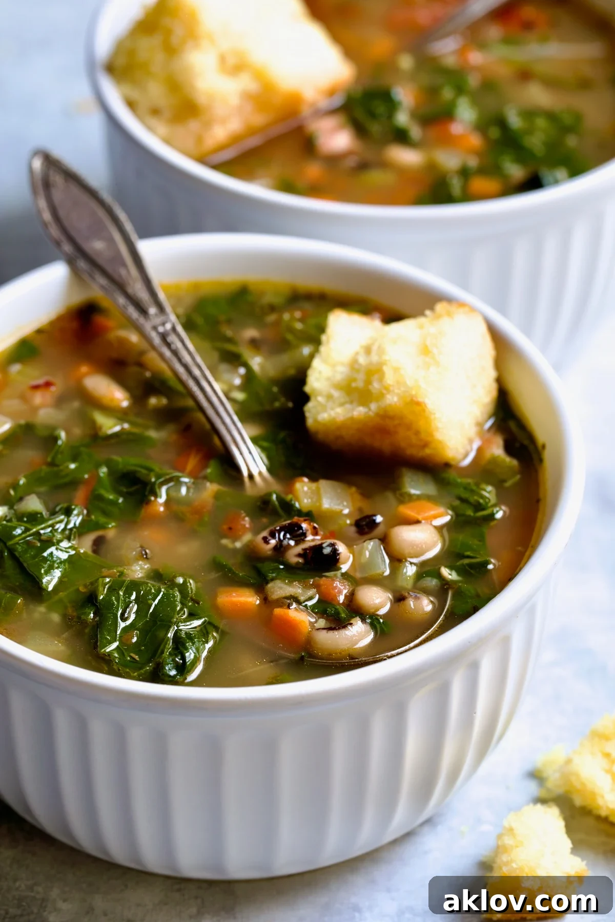Two servings of Black-Eyed Pea Soup in white bowls with cornbread on top.