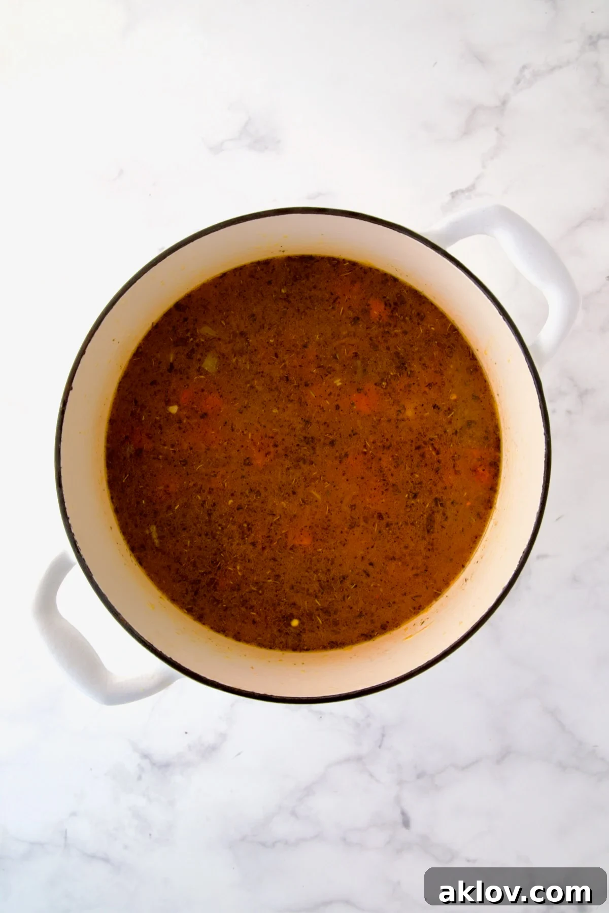 Broth and tomatoes added to cooked vegetables and spices in white Dutch oven.