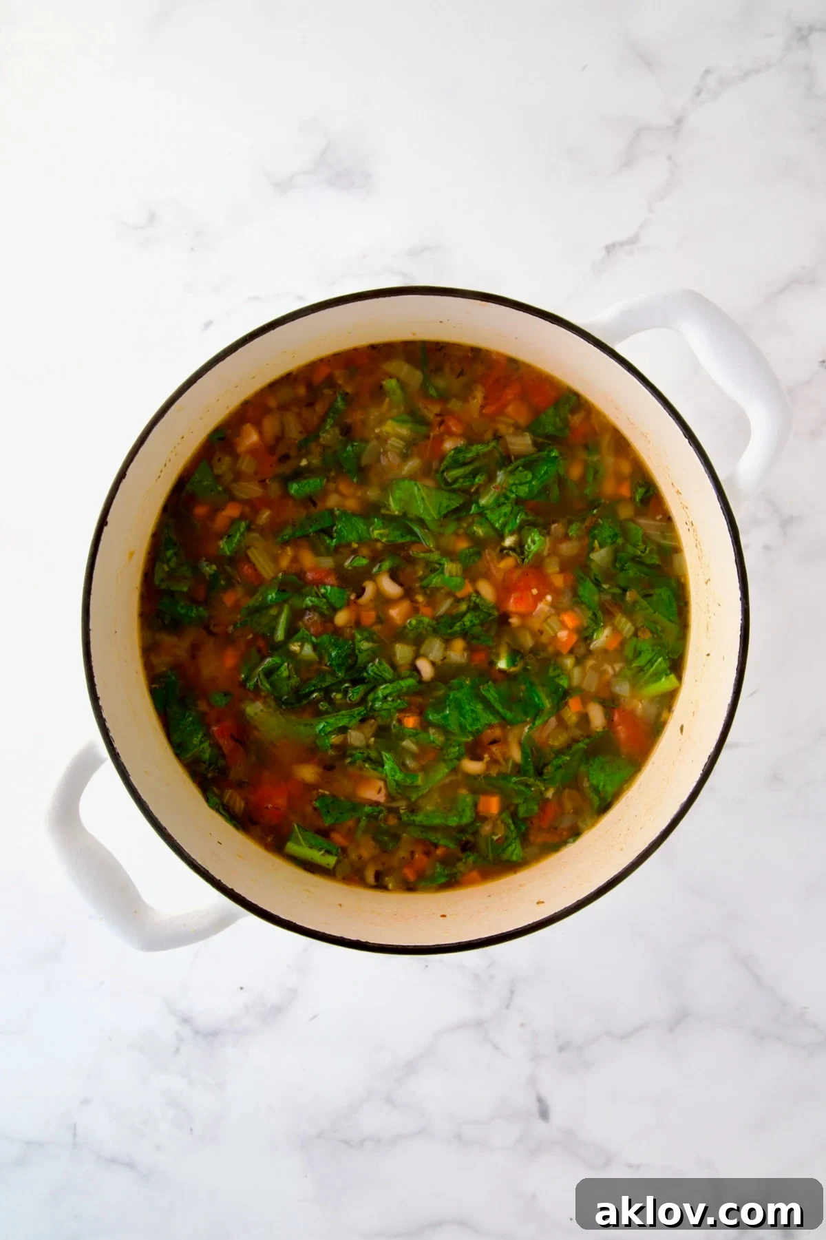 Greens and black-eyed peas added to cooked vegetables, broth, tomatoes and spices in white Dutch oven.