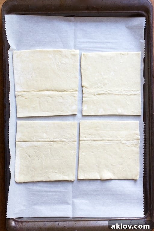 Process photo of four pieces of puff pastry on parchment paper-lined baking sheet.