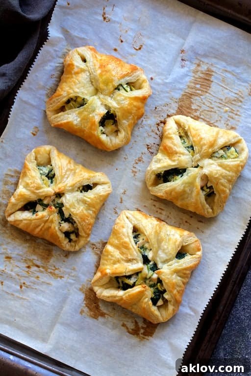 Photo of four baked Chicken, Spinach and Artichoke Puff Pastry Parcels on parchment paper-lined baking sheet.