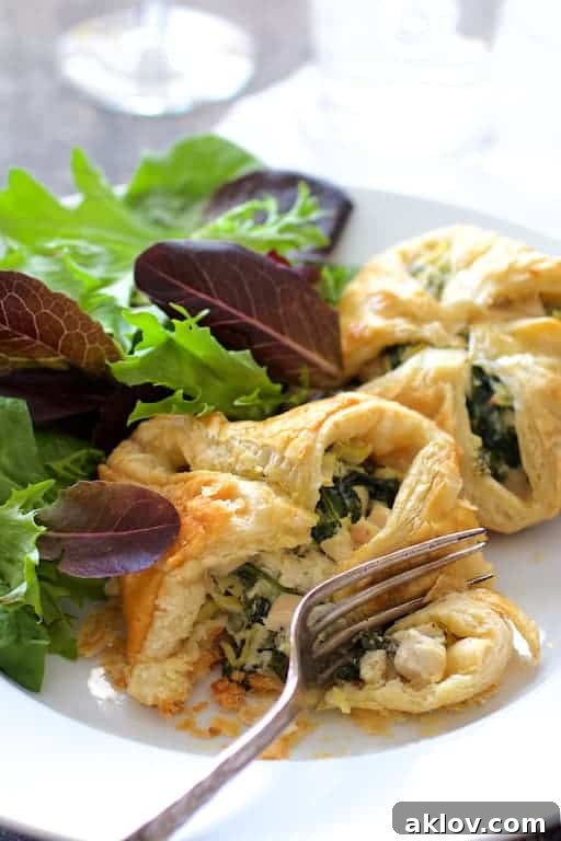 Photo of Chicken Spinach and Artichoke Puff Pastry Parcels on white plate cut into with a fork.