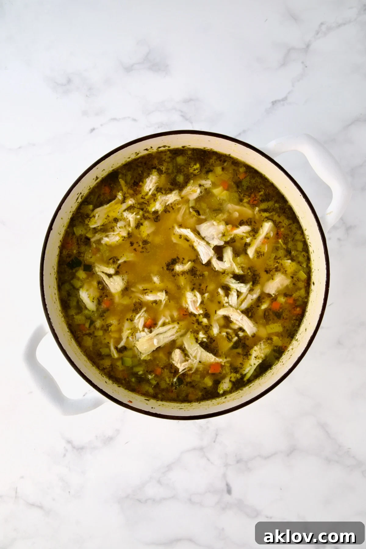 Chicken added to soup in white Dutch oven.