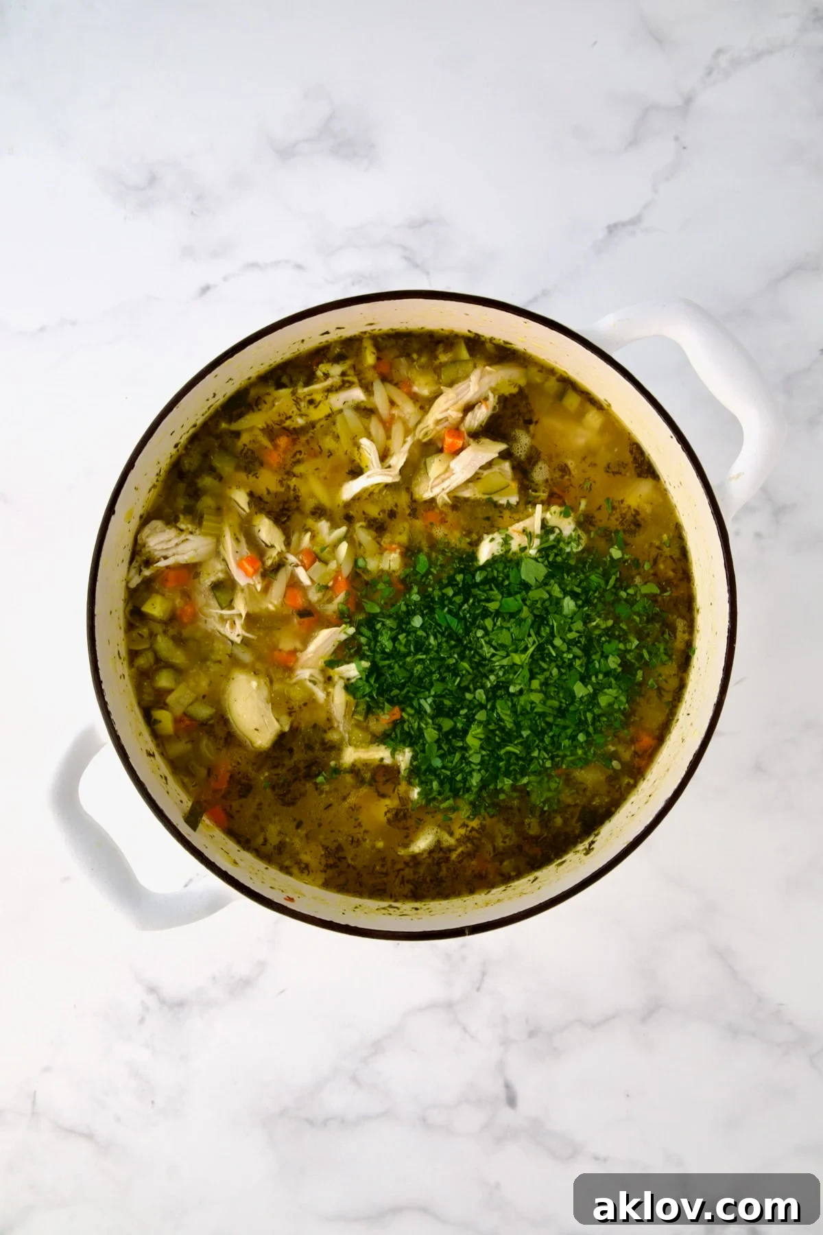 Chopped fresh parsley added to soup in white Dutch oven.