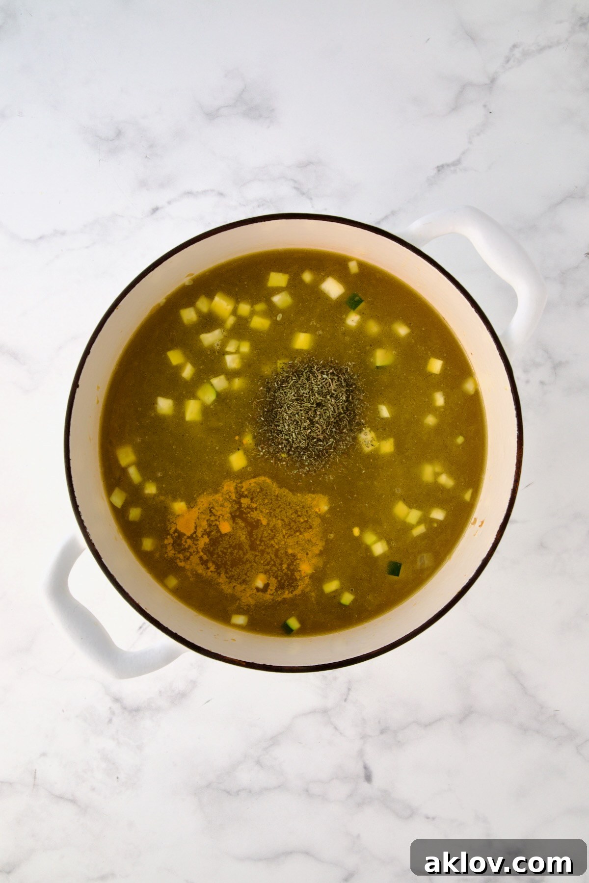 Chicken broth, thyme and turmeric added to vegetables in white Dutch oven.