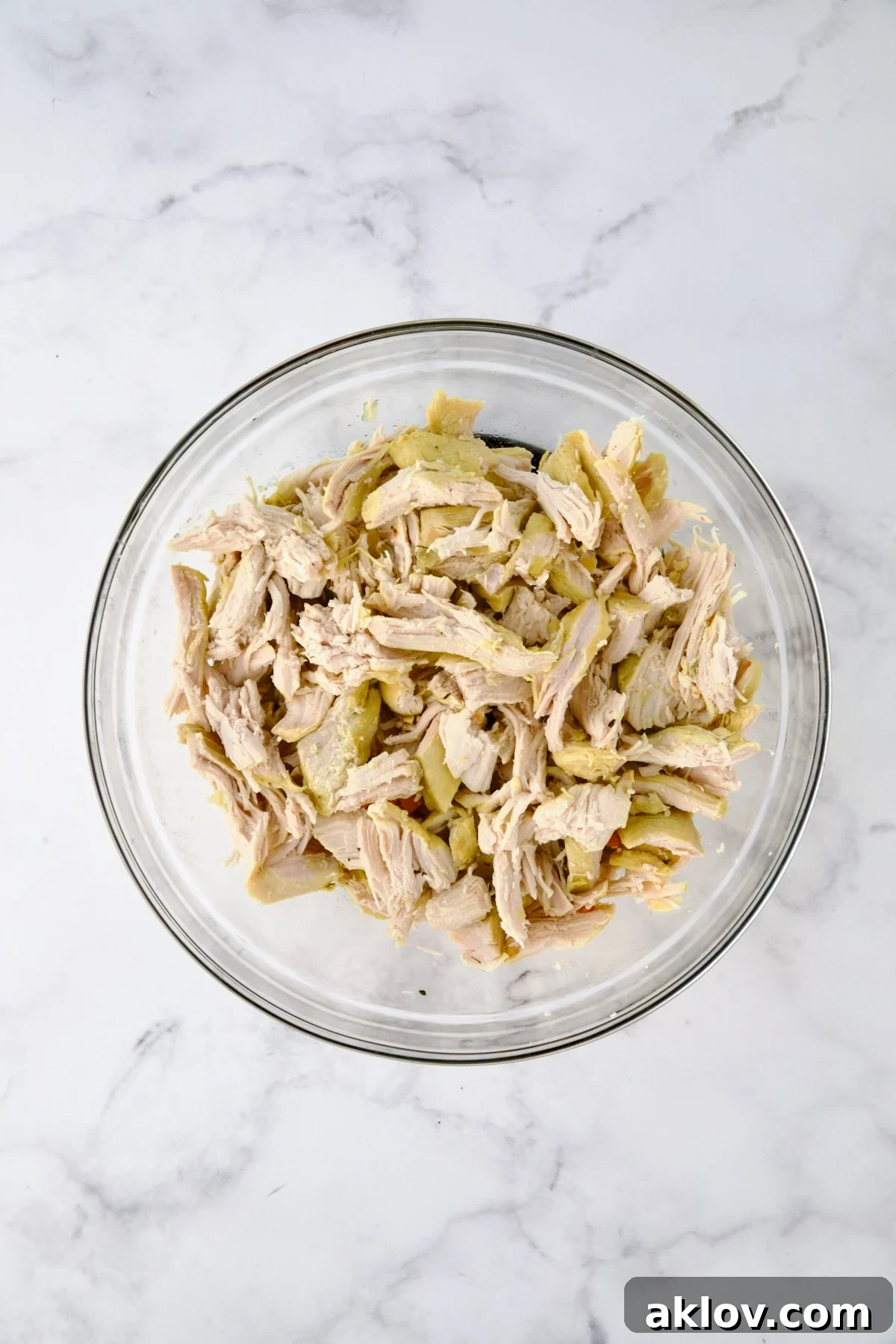 Cooked, shredded chicken in glass bowl.