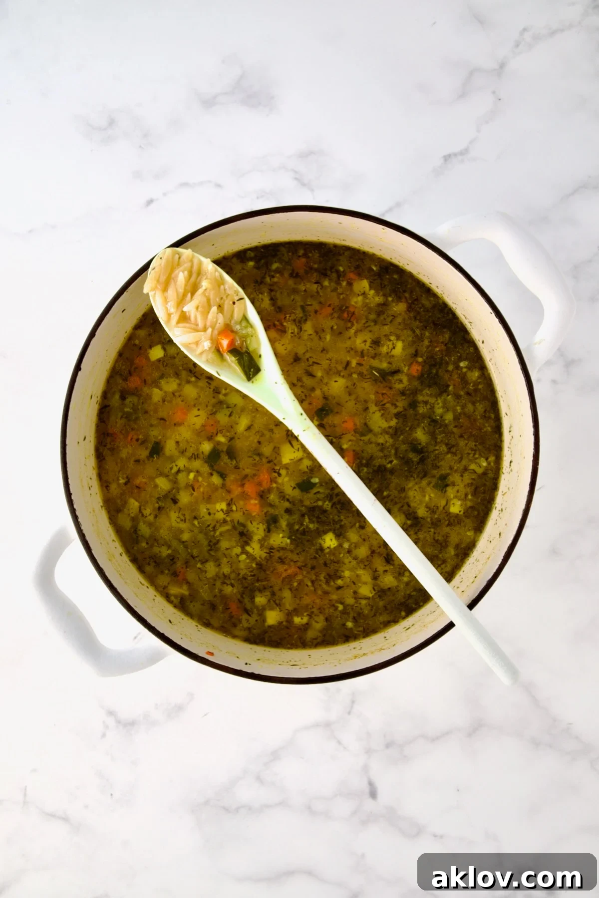 White mixing spoon full of orzo resting on white Dutch oven over soup.