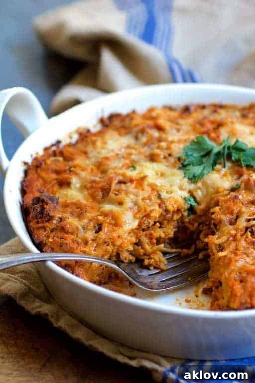 Spaghetti Pie with Three Cheeses in a round white baking dish, presented on a blue striped towel, with a delectable wedge already cut and served.