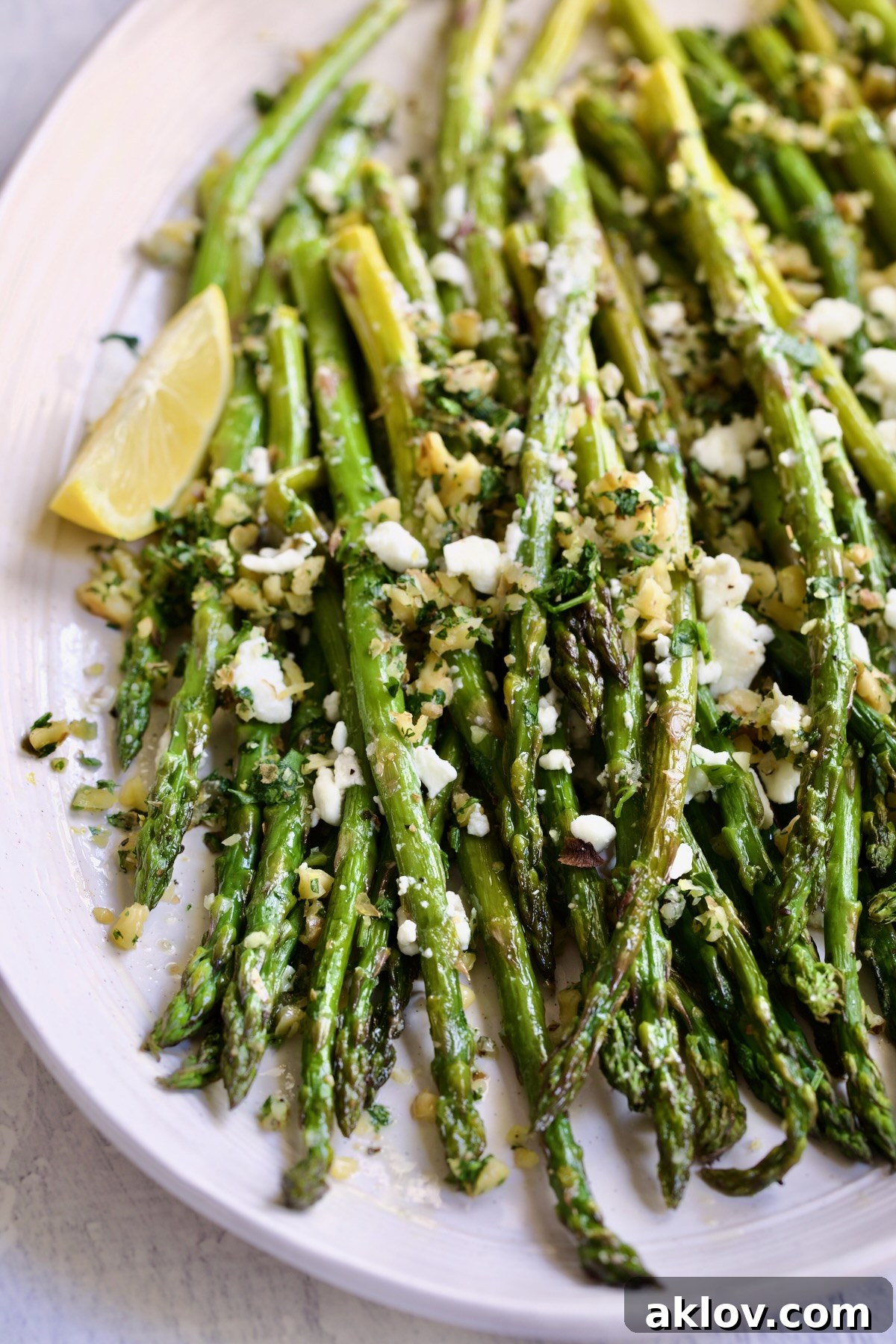 Roasted Asparagus with Walnut Lemon Gremolata and Goat Cheese presented on a white oval platter with a single lemon wedge, ready to be enjoyed.