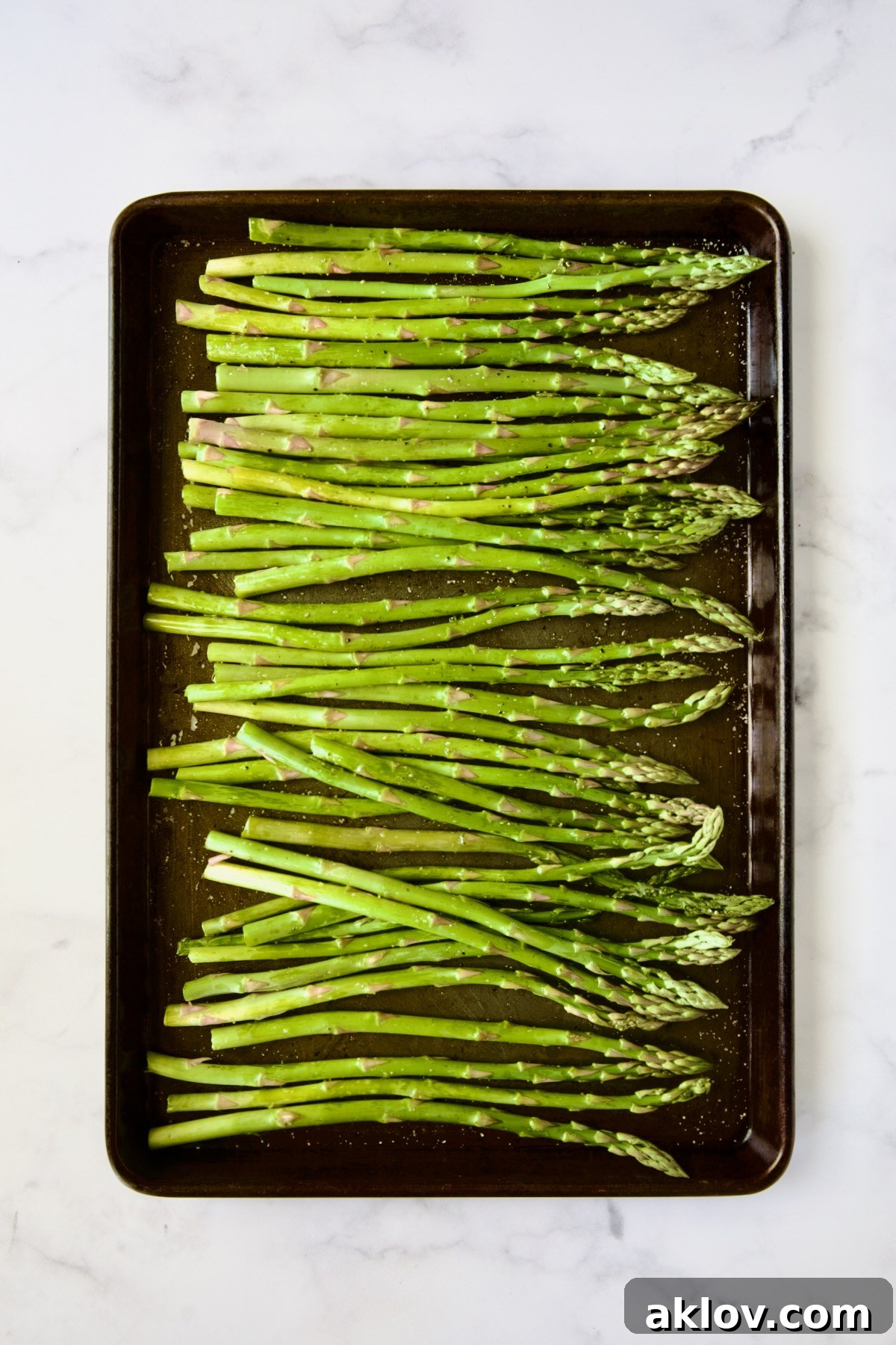 Asparagus spears evenly spread on a rimmed baking sheet, seasoned and ready for roasting.