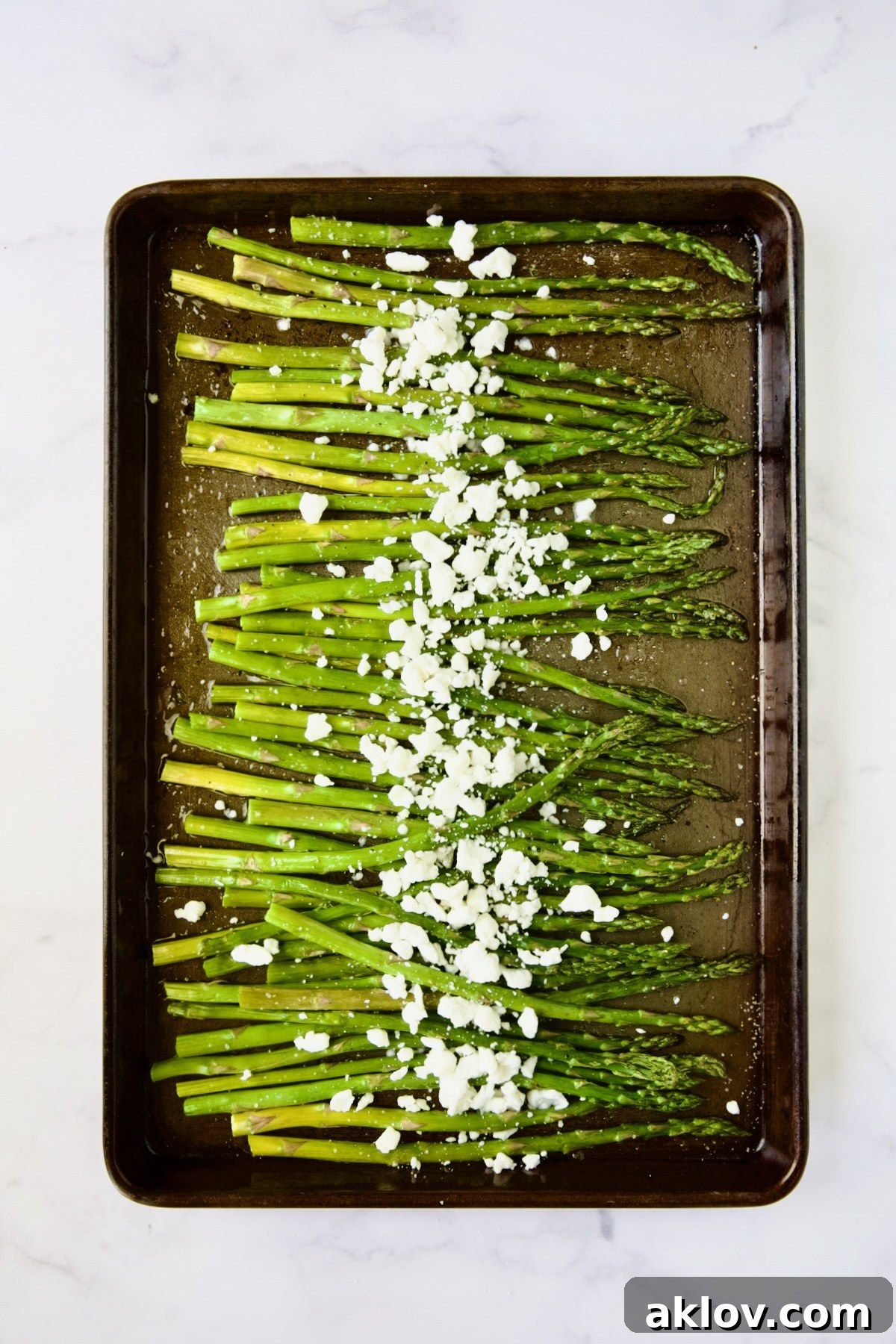 Roasted asparagus lightly sprinkled with crumbled goat cheese, ready for a quick return to the oven.