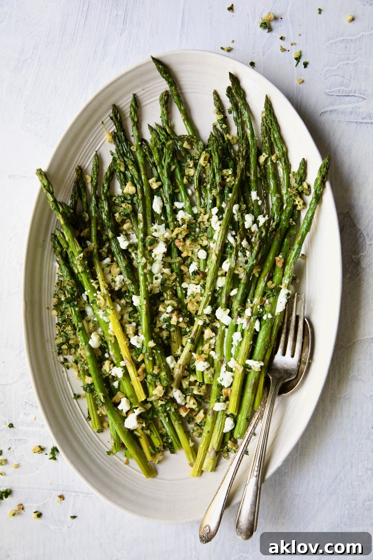A stunning oval platter showcasing Roasted Asparagus adorned with Walnut Lemon Gremolata and Goat Cheese, ready to be served.